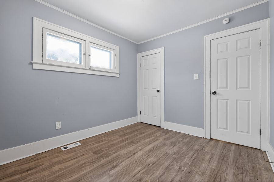 Empty bedroom with light blue walls, white trim, hardwood floors, and two white doors with a small window.