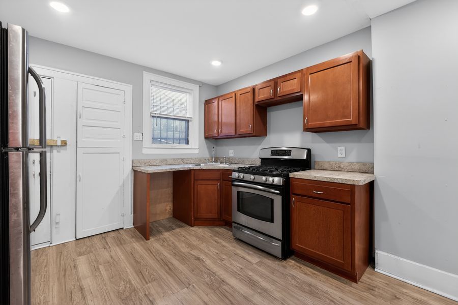 Modern kitchen with cherry wood cabinets, stainless steel gas range, hardwood floors, and recessed lighting.