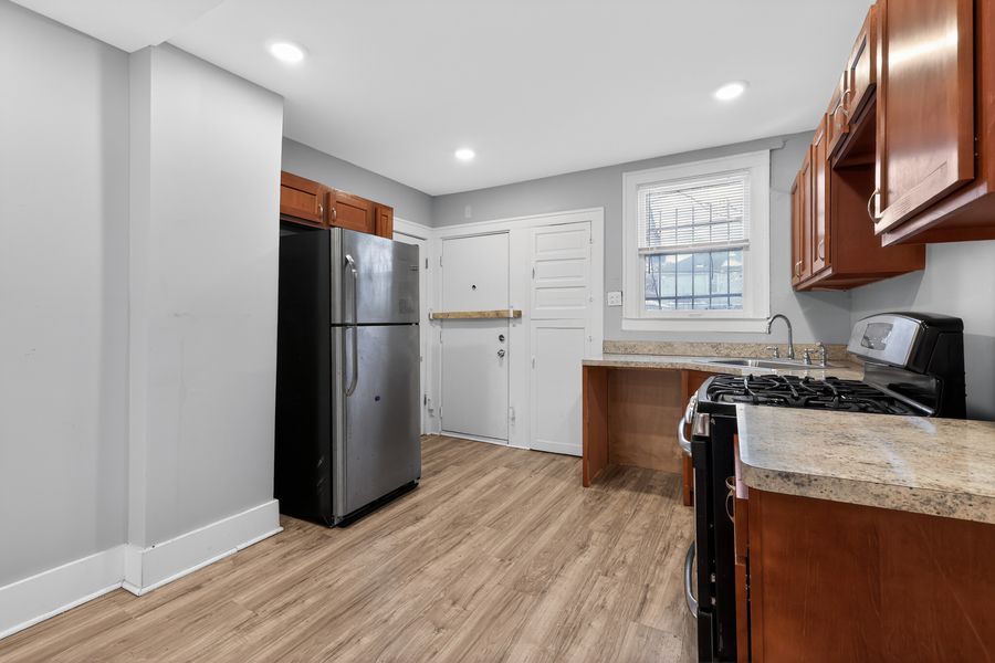 Modern kitchen with stainless steel fridge, gas range, wood cabinets, and light hardwood floors in a bright space.