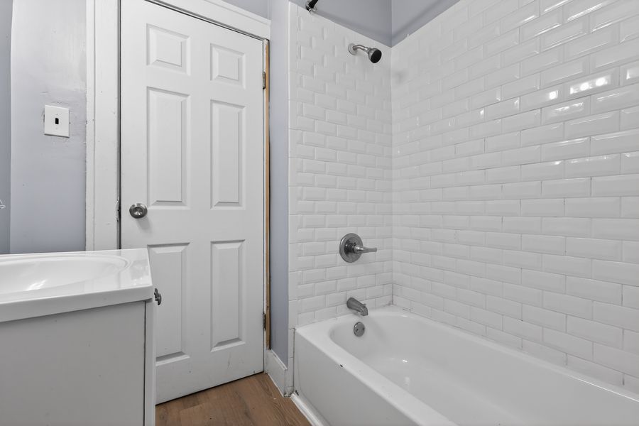White subway tile shower-tub combo with chrome fixtures, white vanity, and wood-look flooring in a bright bathroom.