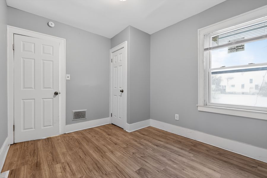Vacant bedroom with light gray walls, hardwood floors, two white doors, and a bright window.