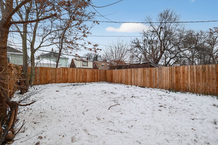 Snow-covered backyard with tall wooden privacy fence and bare trees in winter.