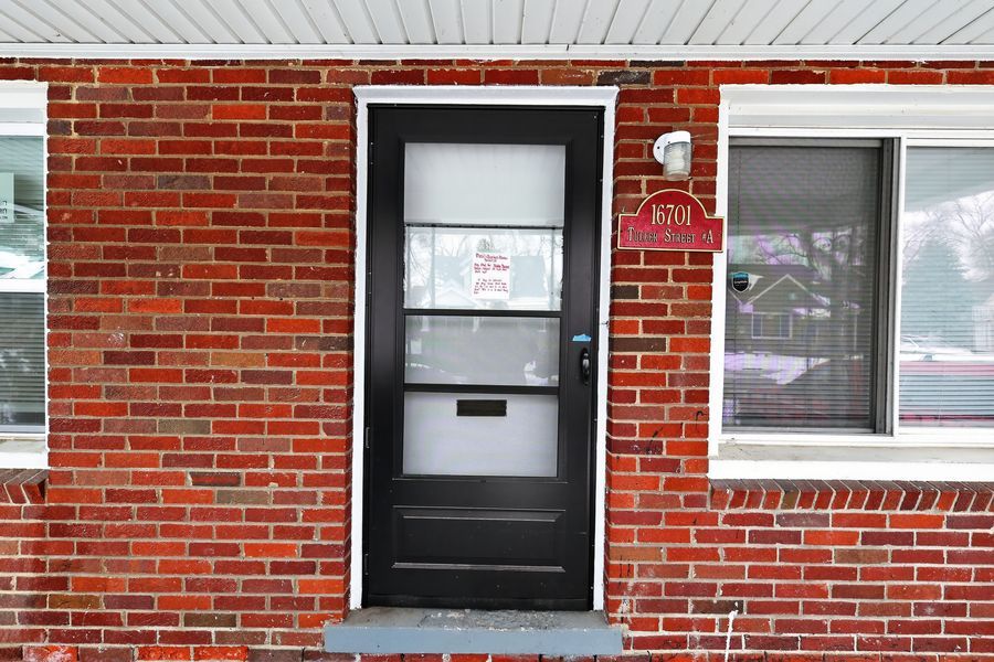 Brick exterior home entrance with black front door, house number plaque, and white trim windows.