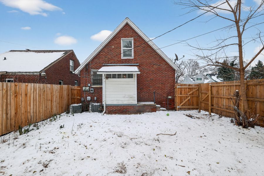 Brick detached garage with white door surrounded by snow and wooden fence.