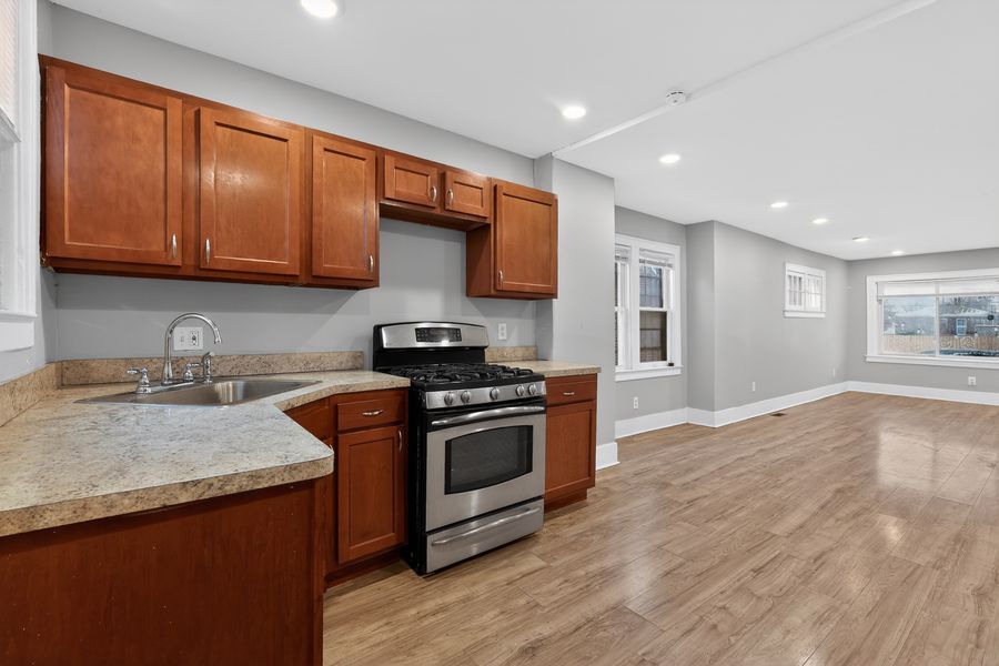 Modern kitchen with wooden cabinets, stainless steel gas range, granite countertops, and hardwood floors.
