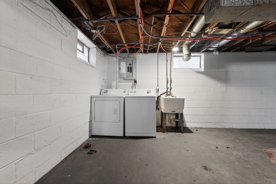 Unfinished basement laundry room with washer and dryer, exposed ceiling pipes, concrete block walls, and utility sink.