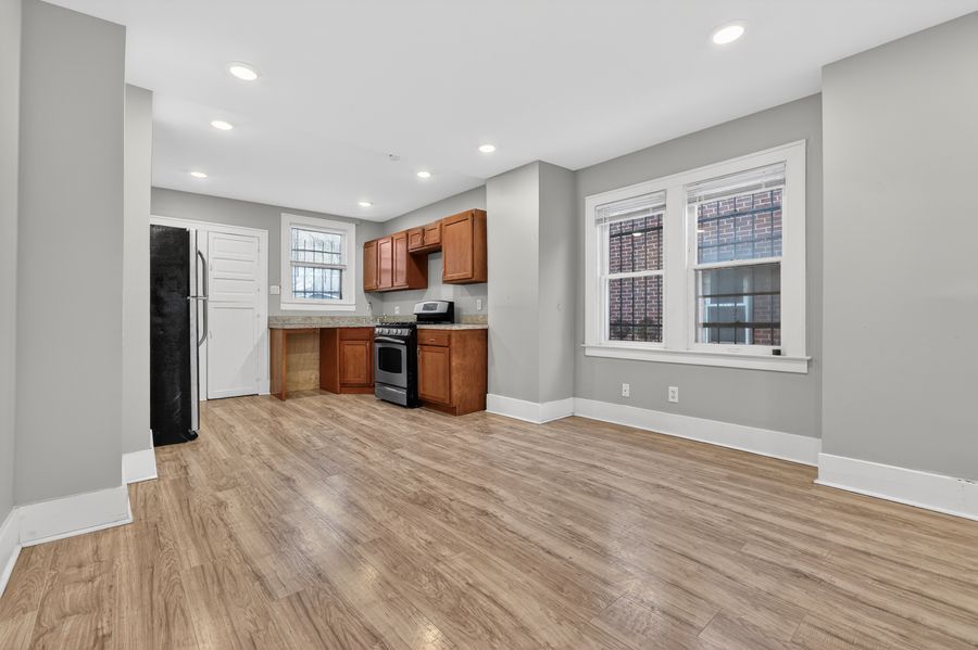 Modern kitchen with hardwood floors, brown cabinets, stainless steel appliances, and large windows in a bright open space.