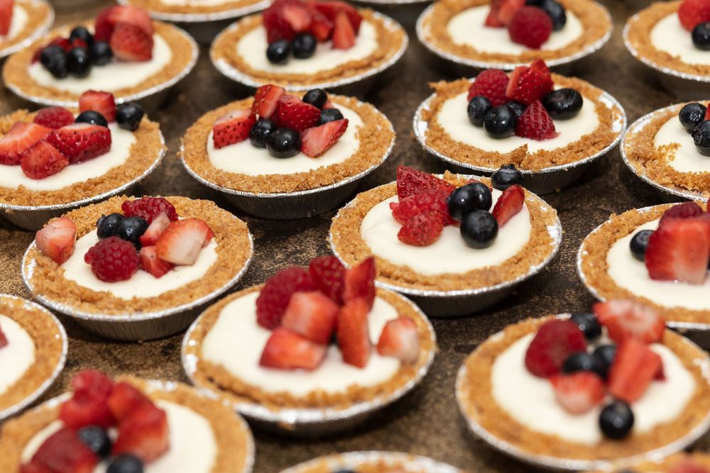 Mini cheesecake tarts with graham cracker crusts topped with fresh strawberries, raspberries, and blueberries.