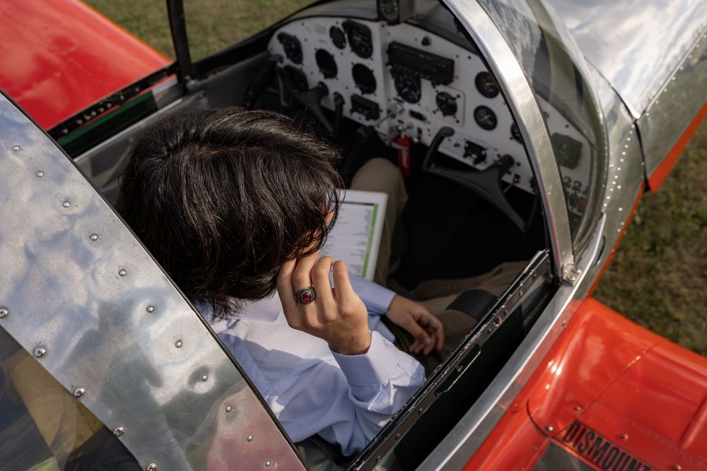 Young pilot studying checklist in red small aircraft cockpit with instrument panel visible from above.