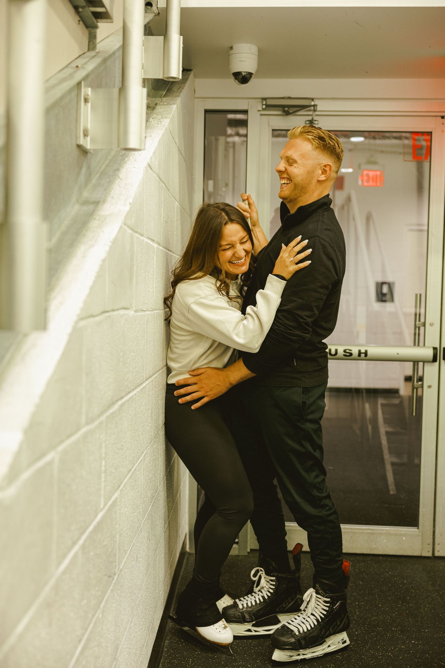 couple laughing against wall entrance to ice skating rink for Fort Lauderdale engagement shoot