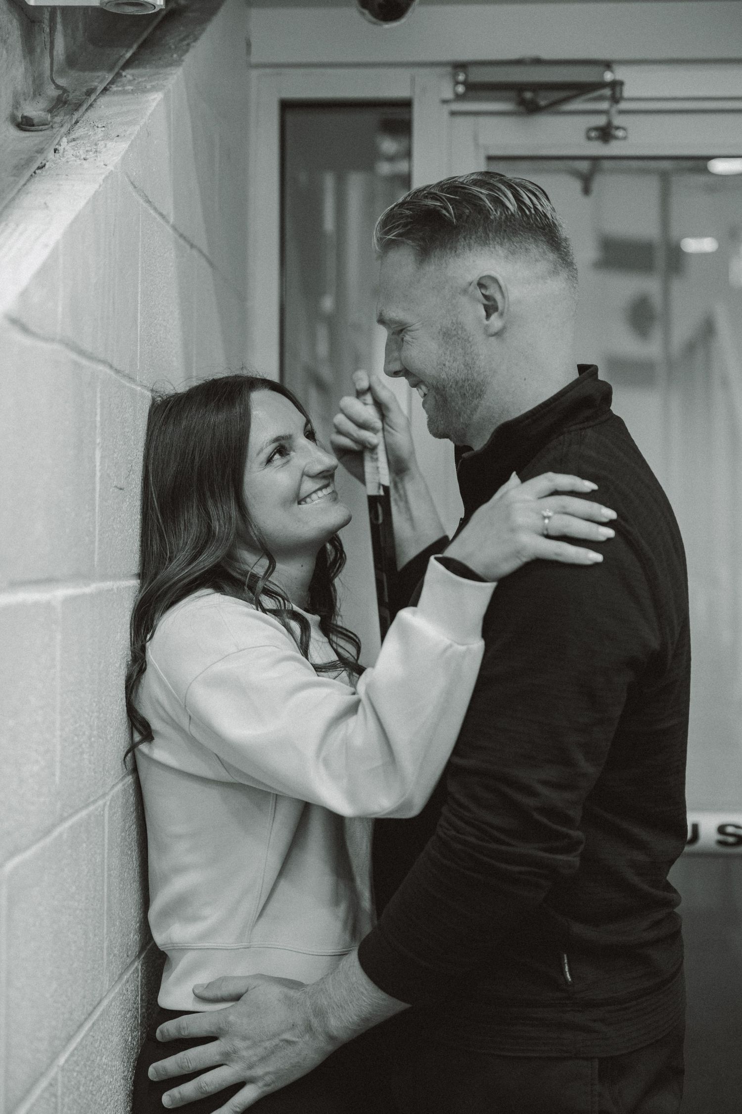 couple staring into each others eyes against wall entrance to ice skating rink for engagement shoot in broward county