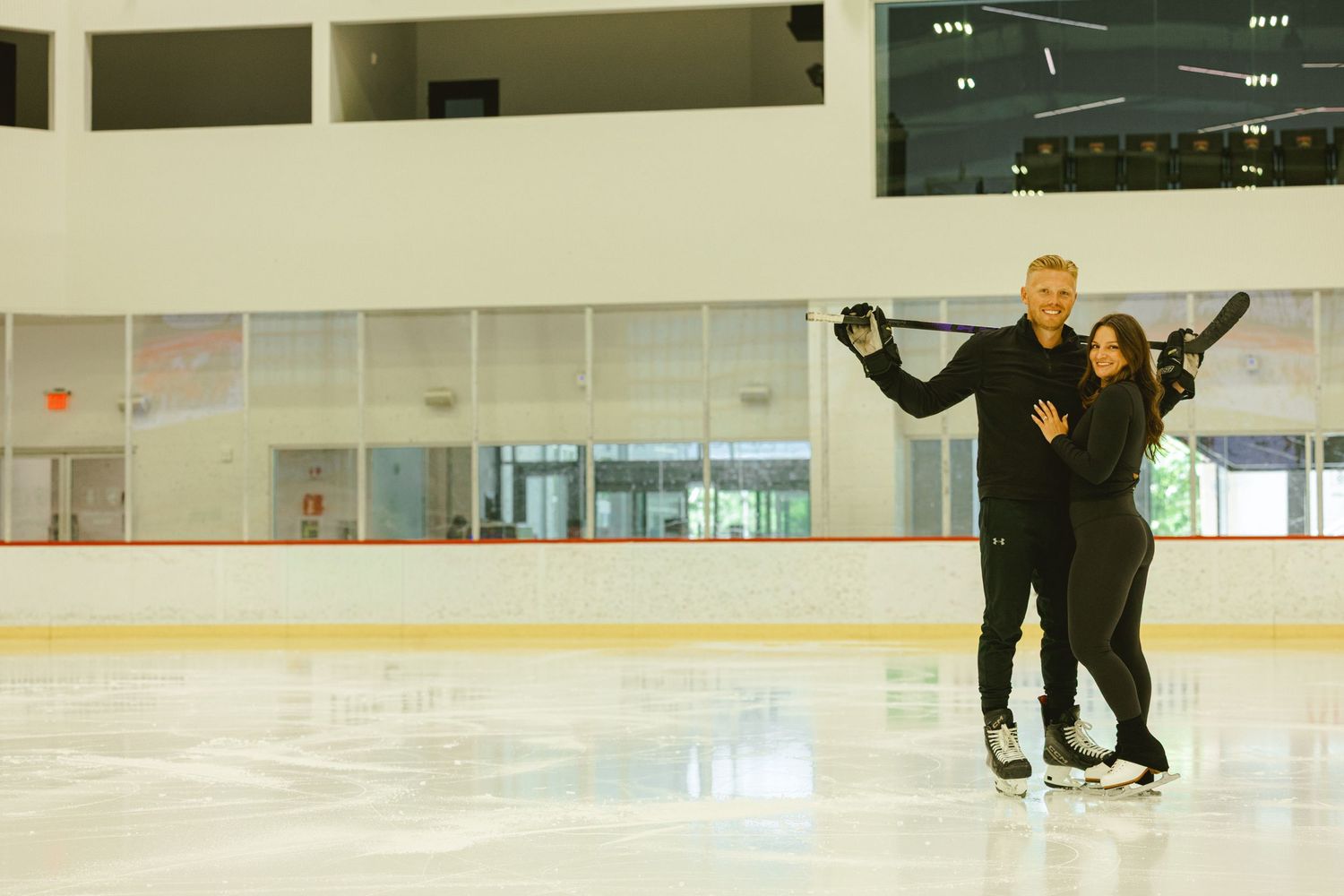 engagement couple posing with hockey stick on ice rink