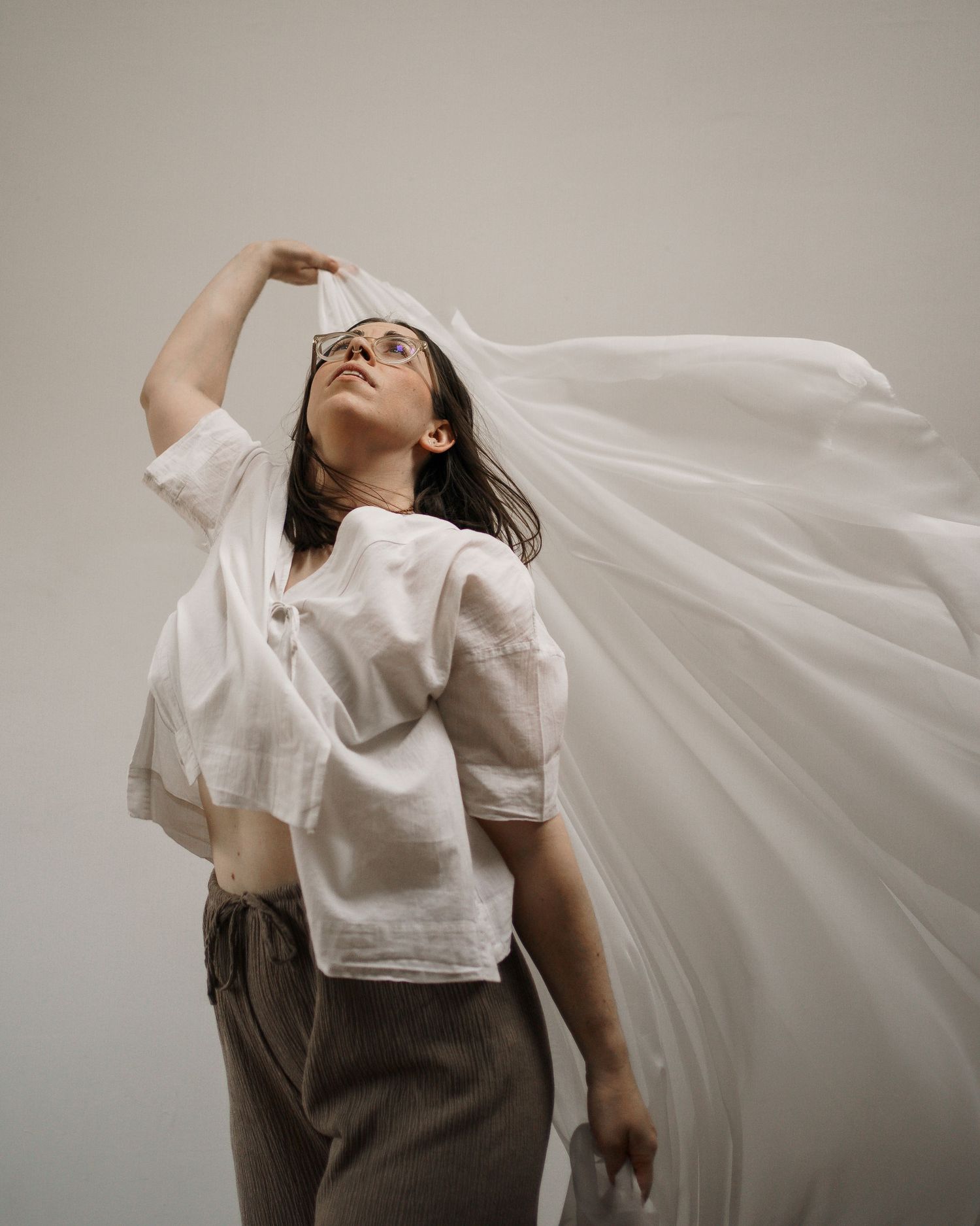 Woman in white shirt with flowing white fabric blowing in the wind against a neutral background.