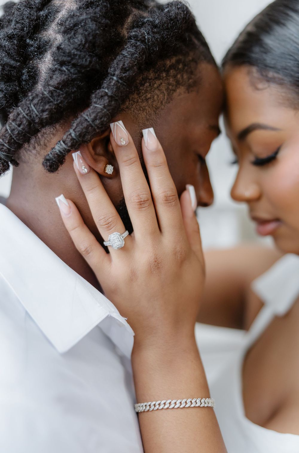 Close-up of engagement ring on bride's hand as couple touches foreheads together tenderly.