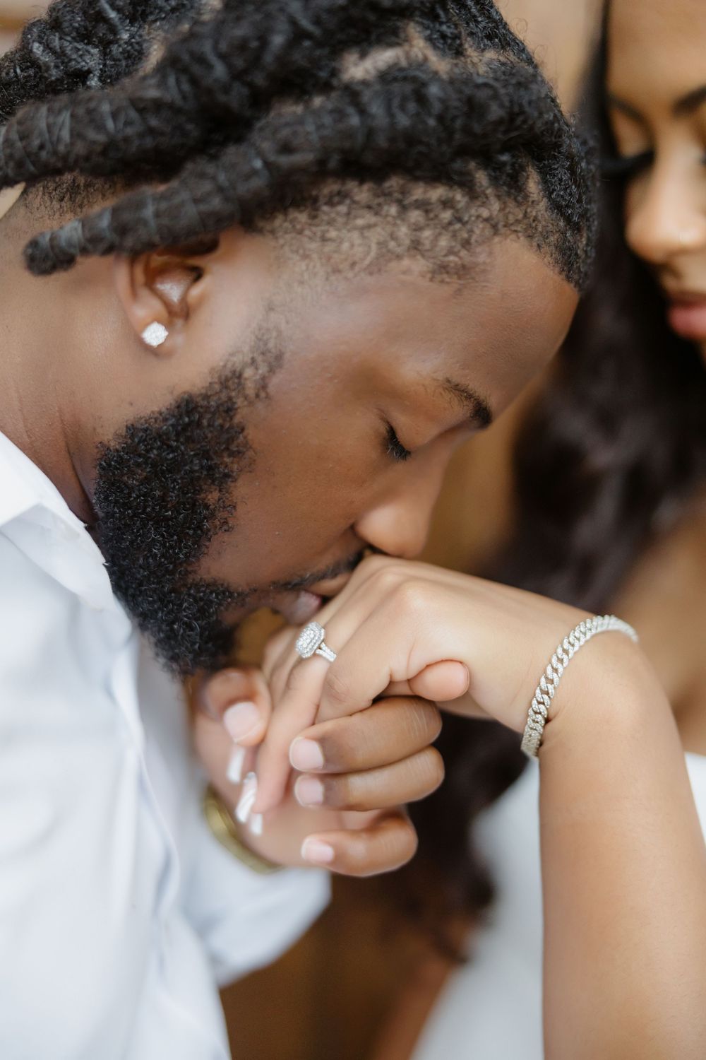 Groom tenderly kisses bride's hand adorned with diamond ring and silver bracelet during romantic wedding moment.