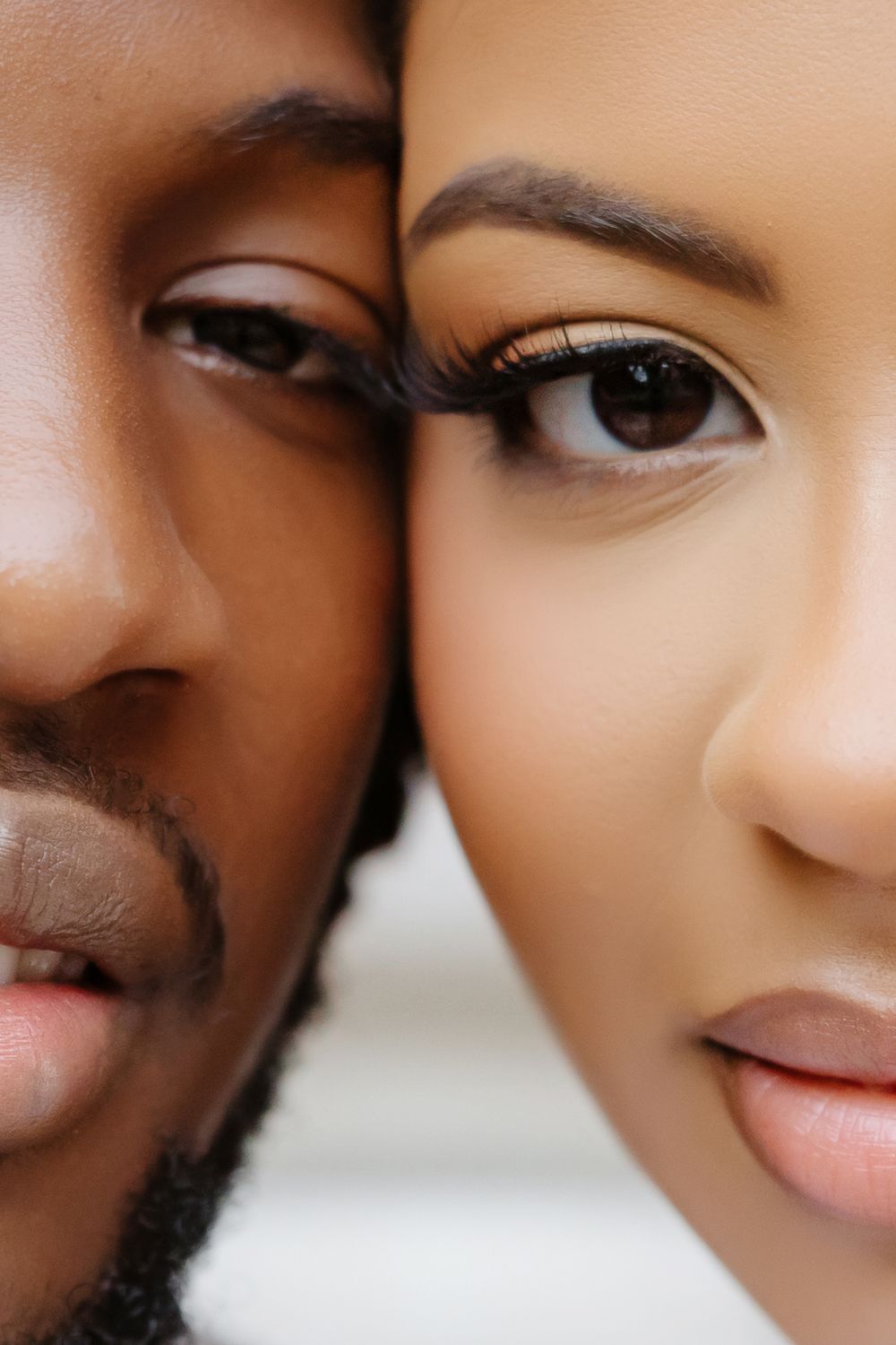 Close-up portrait of a Black man and a light-skinned woman with dramatic eye makeup, faces side by side.