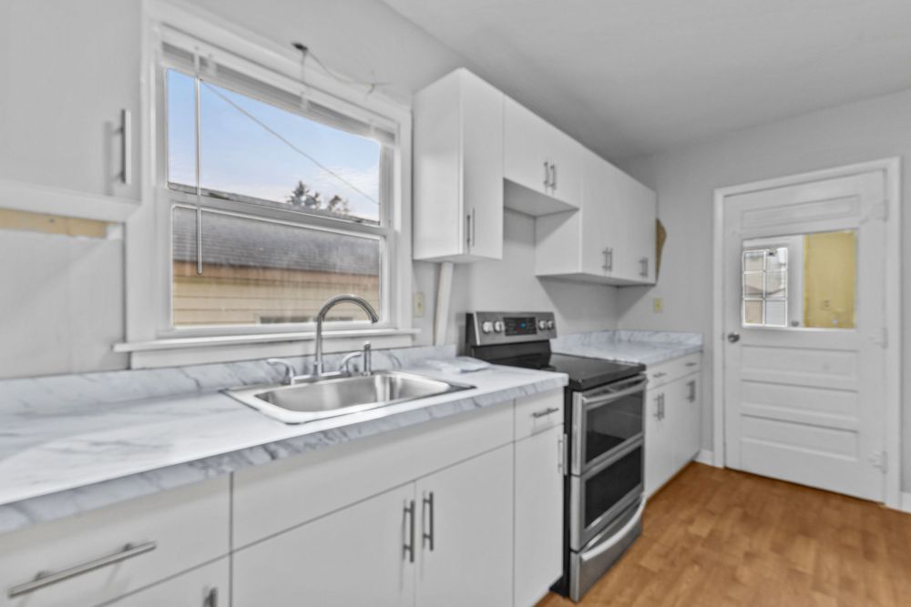 Bright kitchen with white cabinets, stainless steel sink, double oven range, and marble countertops.