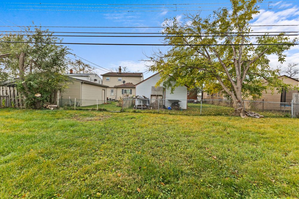 Spacious backyard with lush green lawn, mature tree, wooden deck, and fenced perimeter.