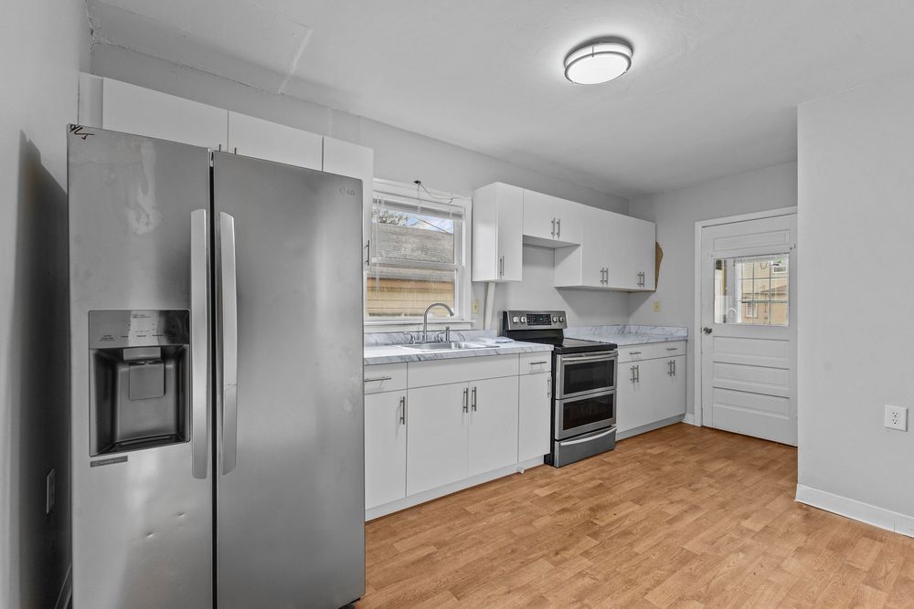Modern kitchen with white cabinets, stainless steel appliances, marble countertops, and light hardwood floors.