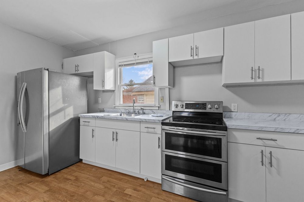 Updated kitchen featuring white shaker cabinets, stainless steel refrigerator, double oven range, and marble counters.