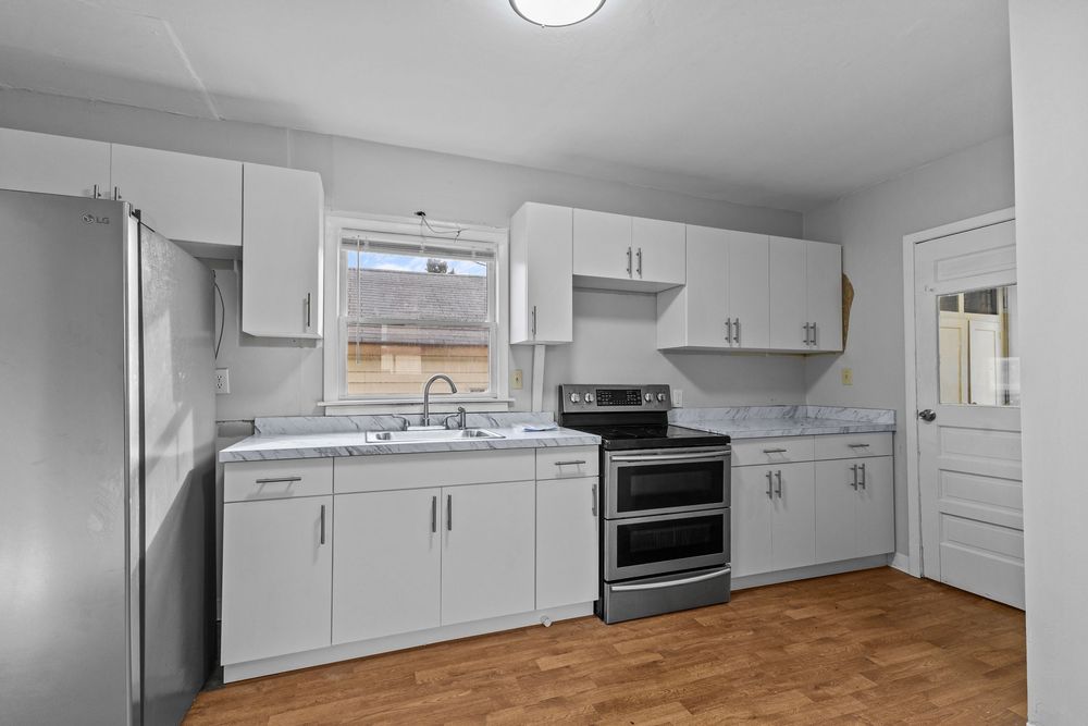 Clean white kitchen with stainless steel appliances, marble-look countertops, and light wood flooring.
