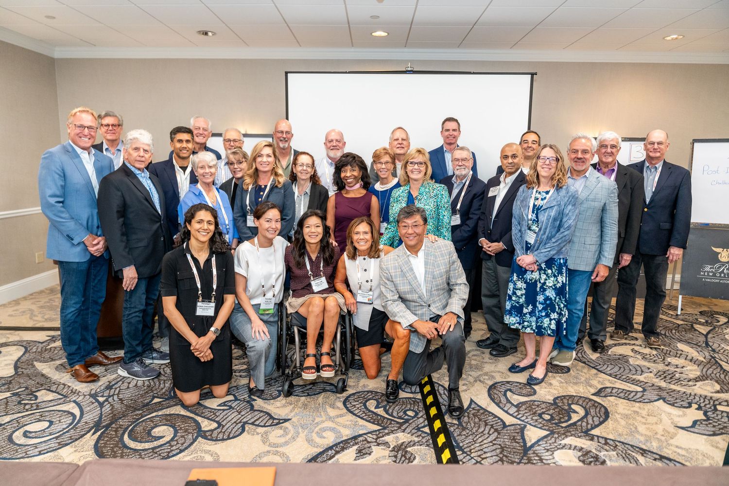 Large group of professionals posing together in a conference room for a formal group photo at a business event.
