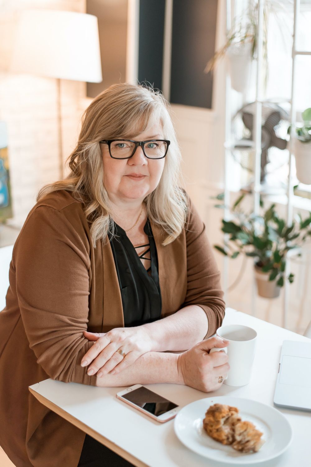 Person in brown cardigan sitting at table with coffee and laptop.