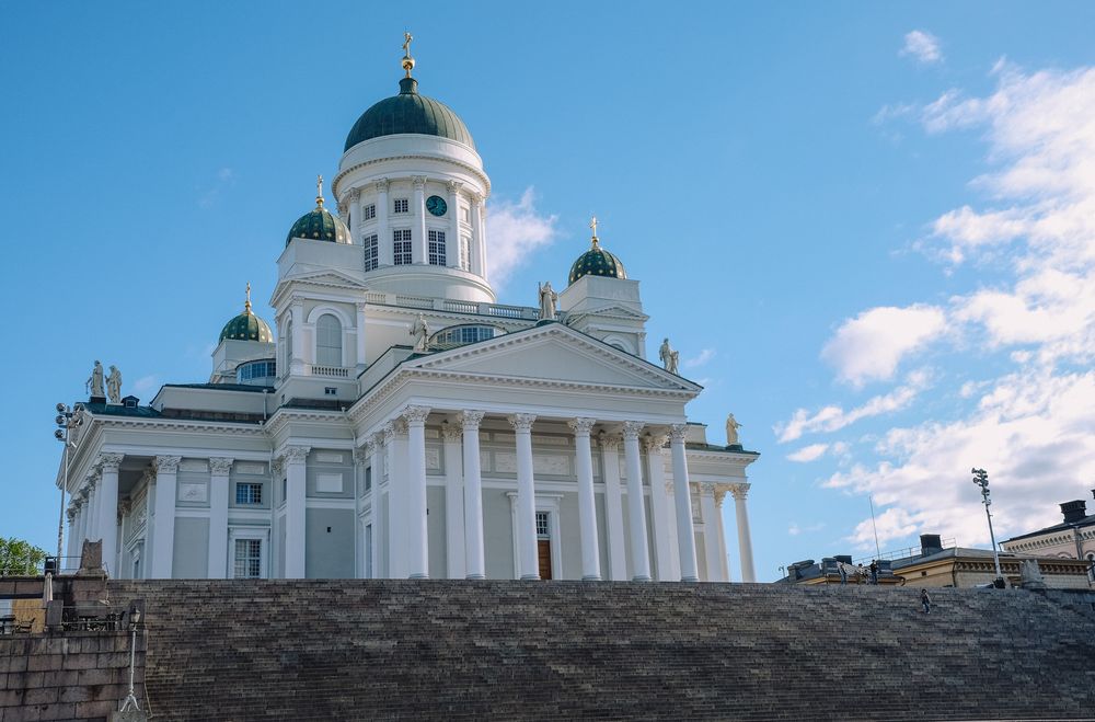 Helsinki Cathedral's white neoclassical facade with green domes stands majestically against a bright blue sky.