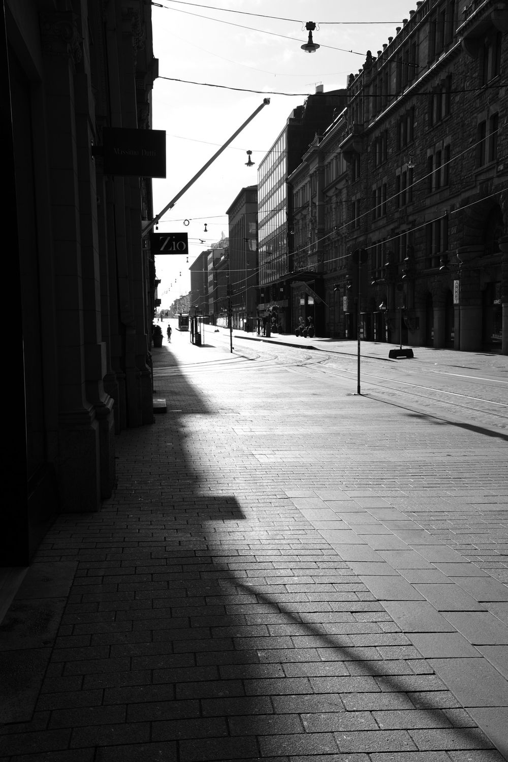 Black and white image of a sunlit empty urban street with tram lines and long shadows at dawn.