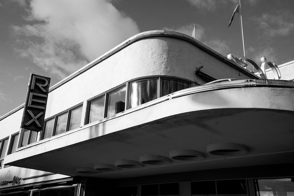 Black and white photo of the Art Deco Rex cinema building featuring curved architecture and bold signage.