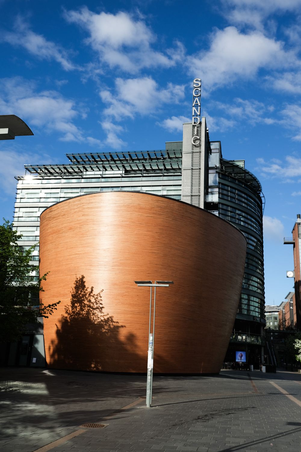 Scandic hotel with unique curved copper facade against blue sky in modern urban setting.