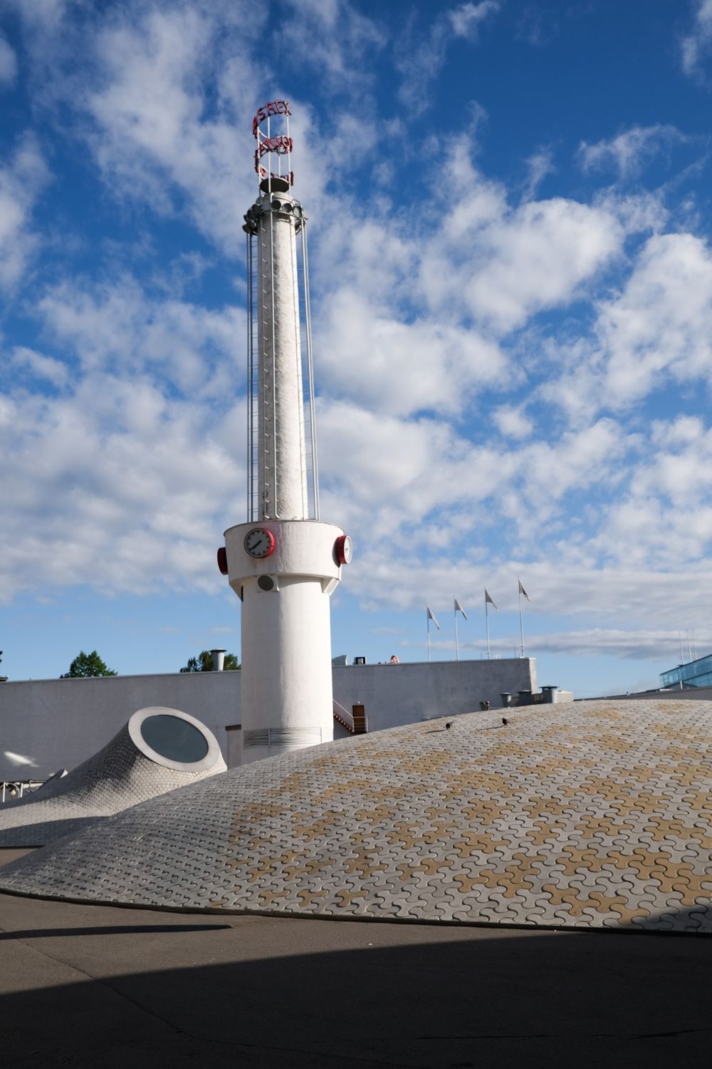 A tall white cylindrical tower with instruments rises from a mosaic dome structure under a partly cloudy blue sky.