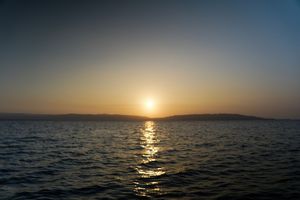 Golden sunset over calm ocean waters with silhouetted distant mountains on the horizon.