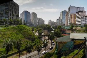 Panoramic view of Lima, Peru skyline with modern buildings, palm trees, and green hillside cliffs on a cloudy day.