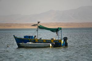 A small blue and yellow fishing boat anchored on calm waters with arid mountains in the background.