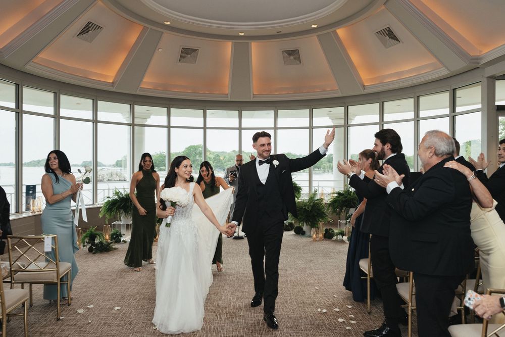 Bride and groom celebrate their wedding recessional in an elegant waterfront venue with guests applauding.