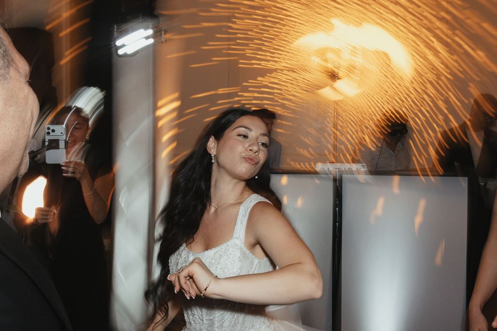 A bride in a white dress dances elegantly at a wedding reception with warm golden lighting.