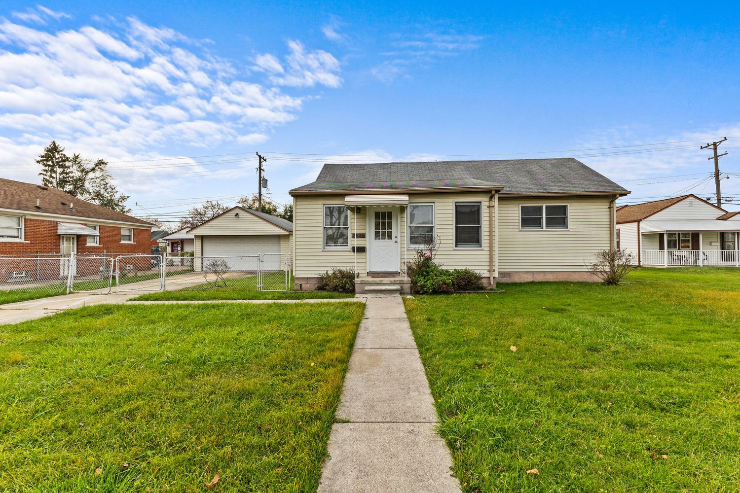 Single-story bungalow with gray siding, green lawn, detached garage, and concrete driveway.