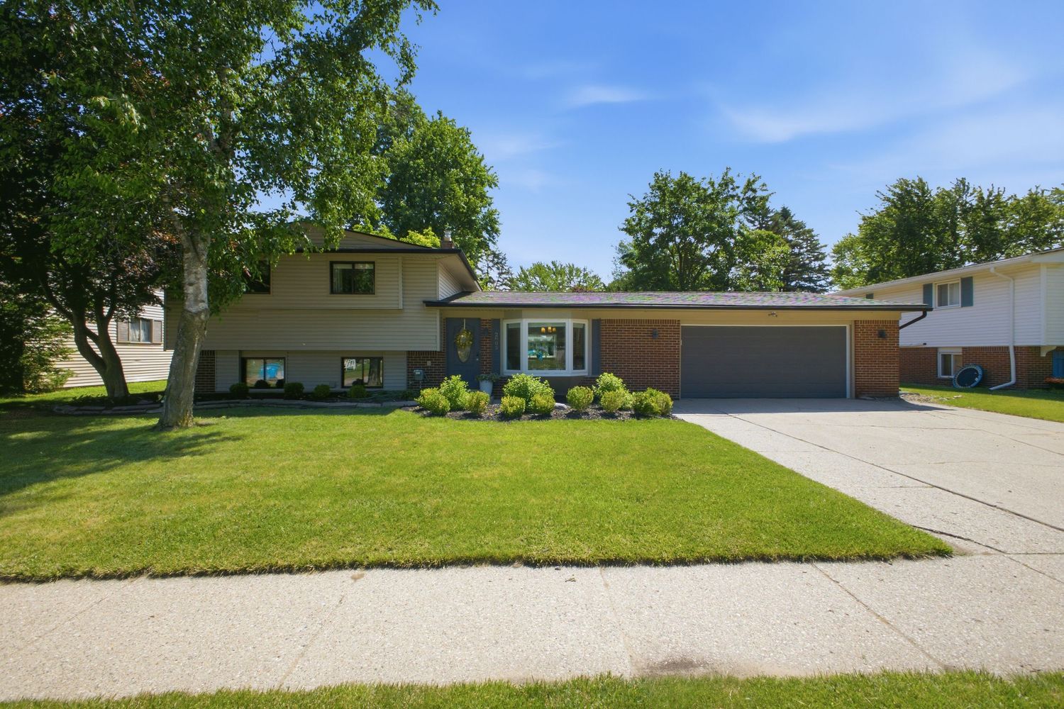 Two-story brick home with covered front porch, lush green lawn, and mature landscaping.