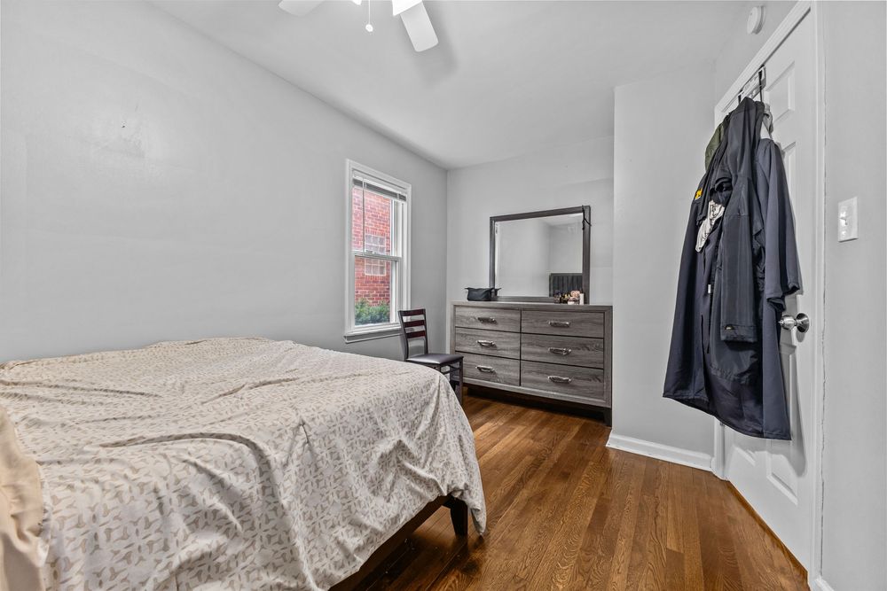 Cozy bedroom with hardwood floors, ceiling fan, dresser with mirror, and natural light from a single window.