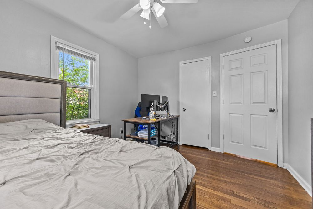 Sunlit bedroom featuring hardwood floors, upholstered headboard, ceiling fan, and a single window.