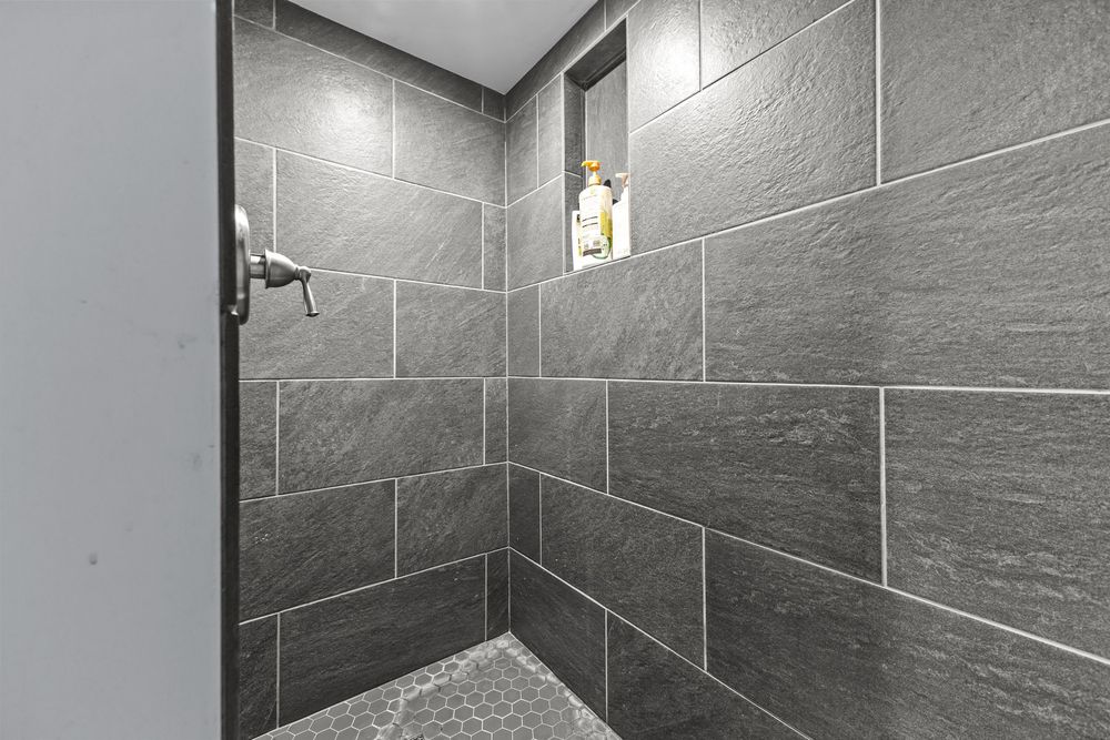 Modern walk-in shower with large gray slate tiles, hexagon mosaic floor, and a built-in niche.