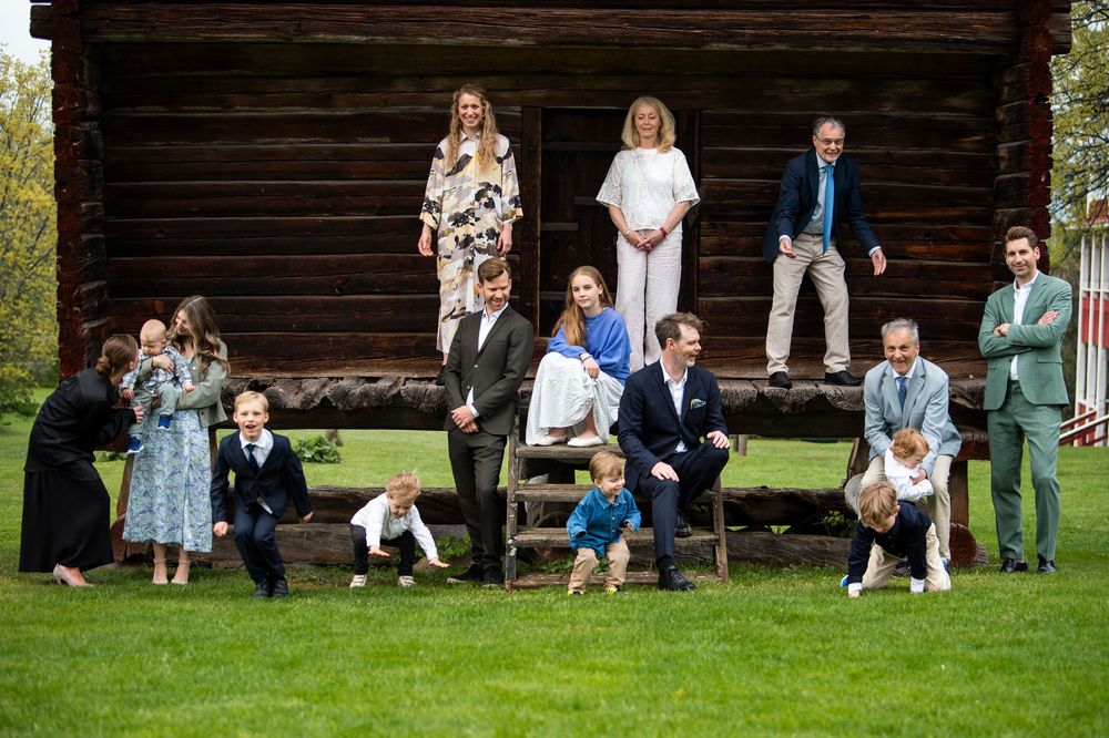Extended family gathering outside a historic wooden building, with adults and children posing casually.