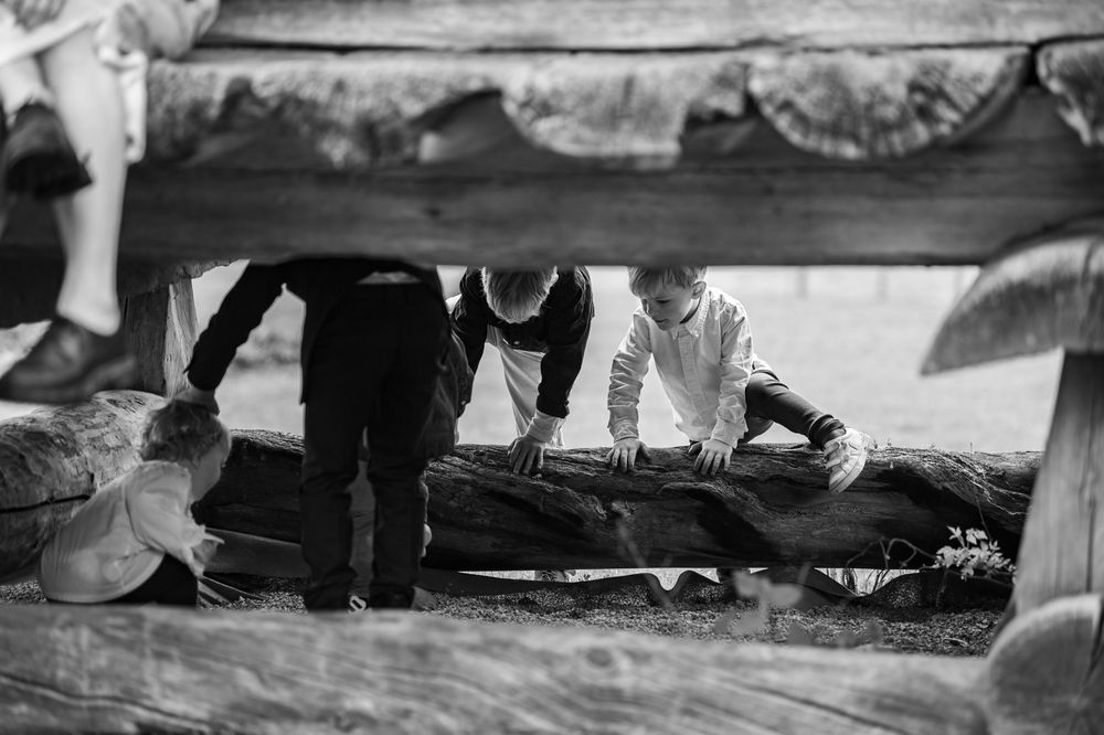 Children playing under a wooden bench with a large log in black and white photo.