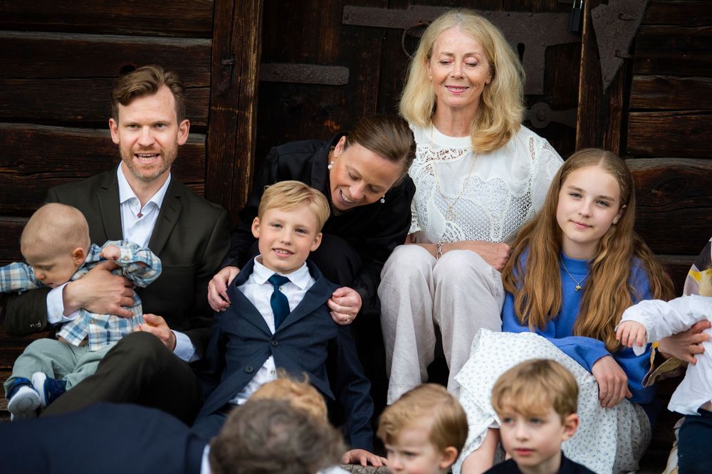 Family portrait on wooden steps featuring two men, children, and a blonde woman in white lace dress.