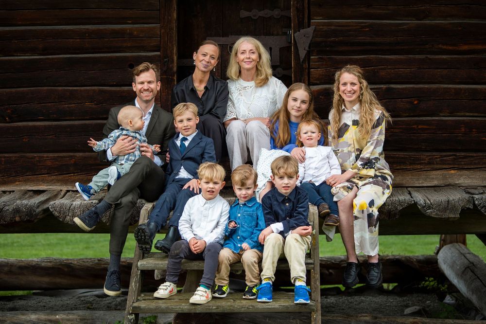 Large family group portrait with grandparents, parents, and children outside a log cabin.