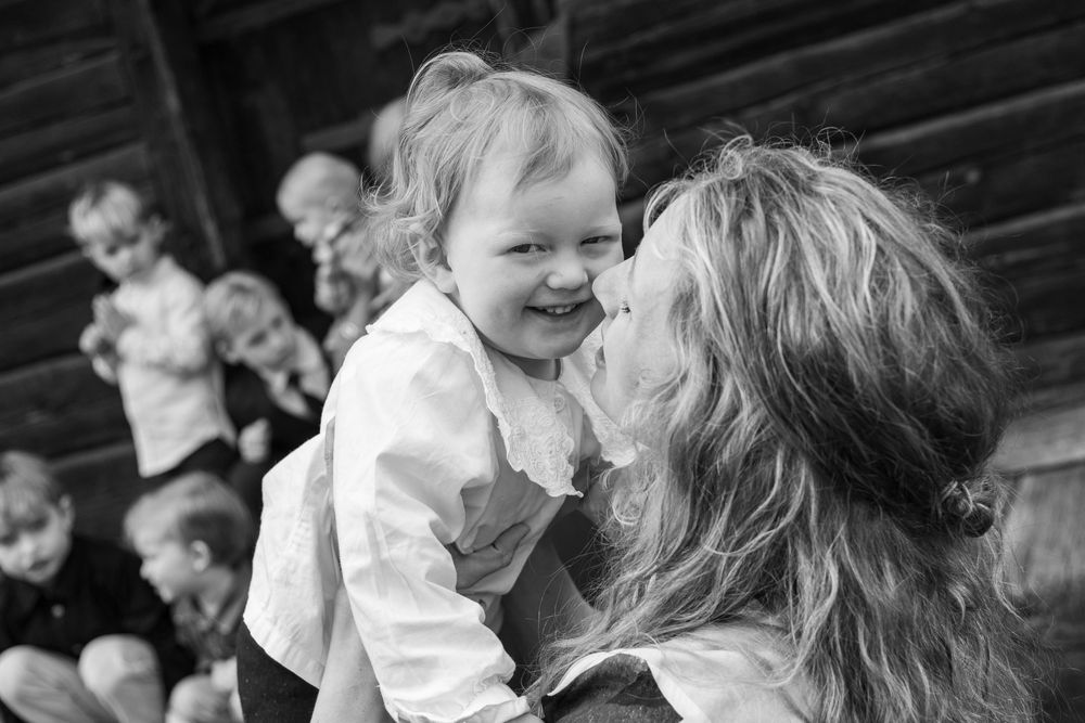 Mother lovingly kissing a laughing toddler girl in black and white family portrait outdoors.