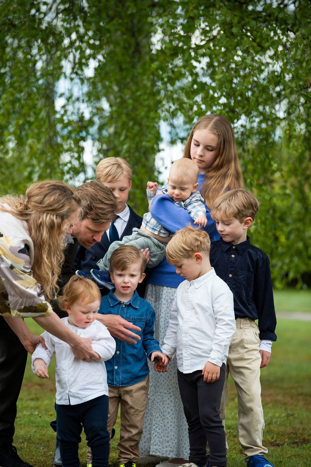 Large family group with parents and six children gathered outdoors under green weeping willow tree.