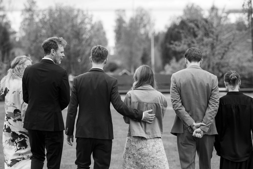 Black and white photo of six adults walking together across a lawn, viewed from behind.