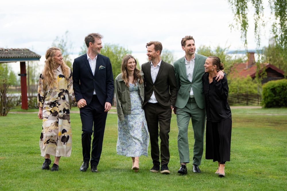 Six young adults walking and smiling together on a green lawn outside on a sunny day.